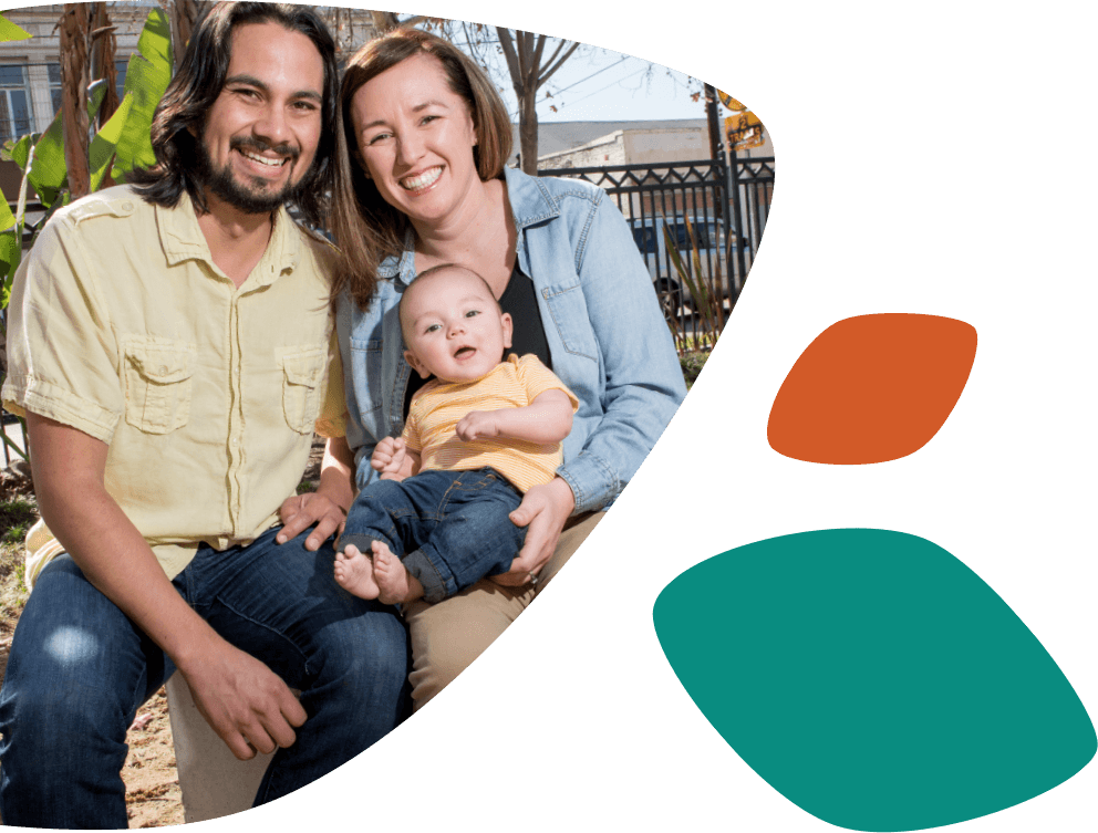 Unos sonrientes padres hispanos sentados con su hijo pequeño, que está sonriendo y sentado en las piernas de la mujer.