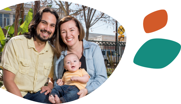 Unos sonrientes padres hispanos sentados con su hijo pequeño, que está sonriendo y sentado en las piernas de la mujer.